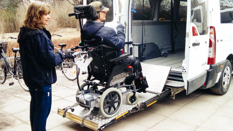 Woman assisting a man on a wheelchair into a van with a lift