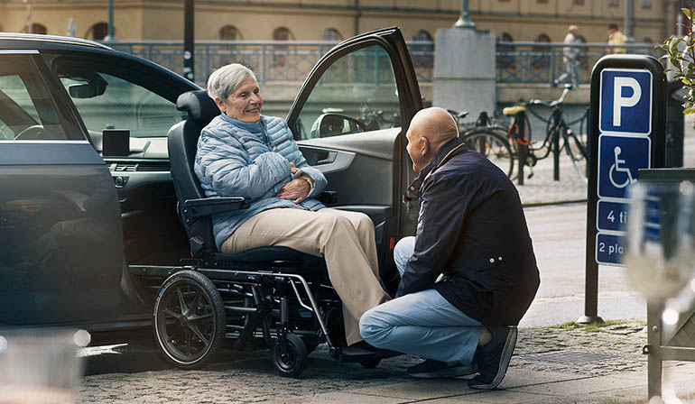 Man assisting woman sitting on a Carony into a car