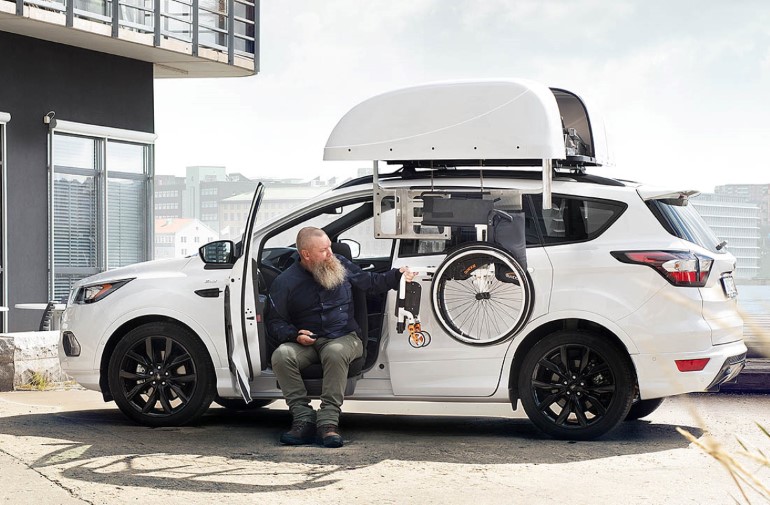 Man retreating his wheelchair from the top of a car with a chair topper