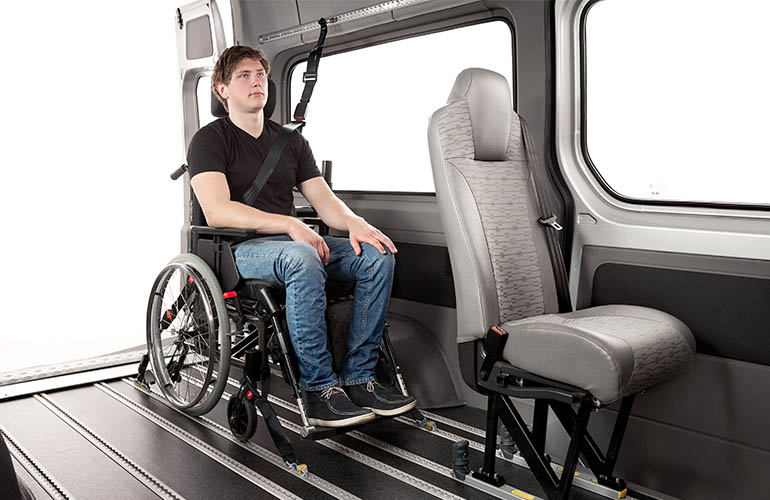Person im Rollstuhl, die mit Personen- und Rollstuhlrückhaltesystemen im Fahrzeug für den Transport gesichert ist