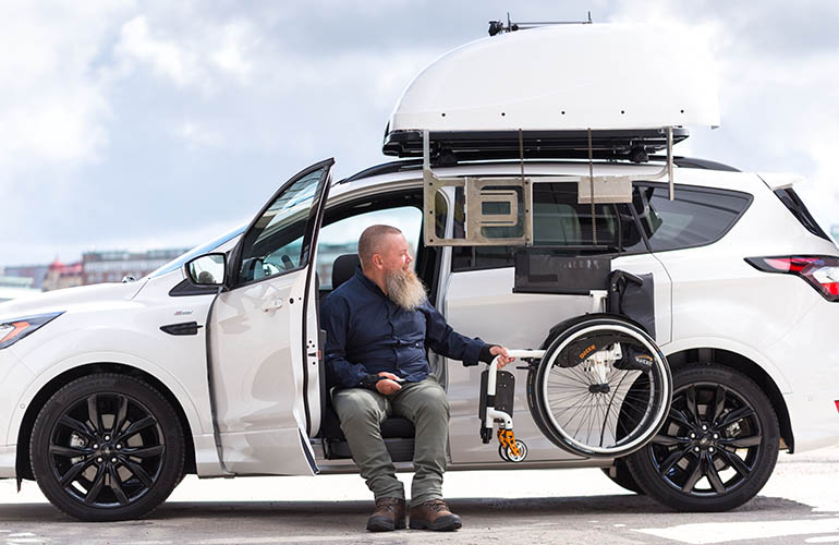 Homme en train de charger son fauteuil roulant dans un coffre de toit Chair Topper sur une voiture