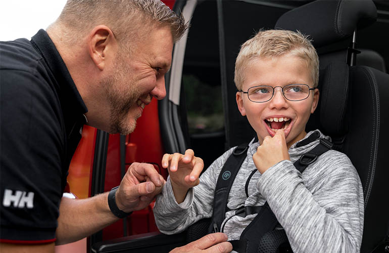 Boy sitting in a vehicle seat and father stands besides him.