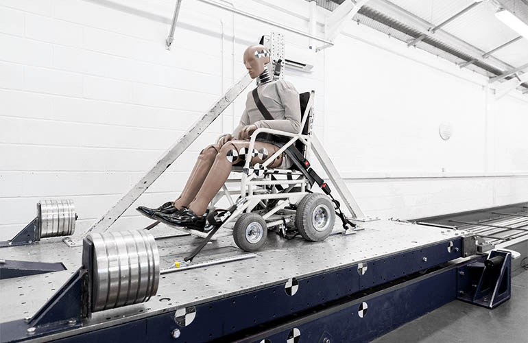 Crashtest-Dummy im zurückgehaltenen Rollstuhl auf einem Crashschlitten