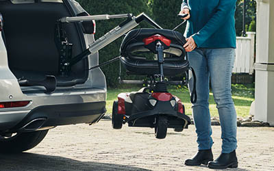 A closeup of the Carolift 100 holding a mobility scooter outside of the boot of a car. 