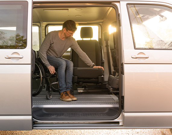 A man transferring from a wheelchair to a 6-way-seat inside of a van with the side door opened. 