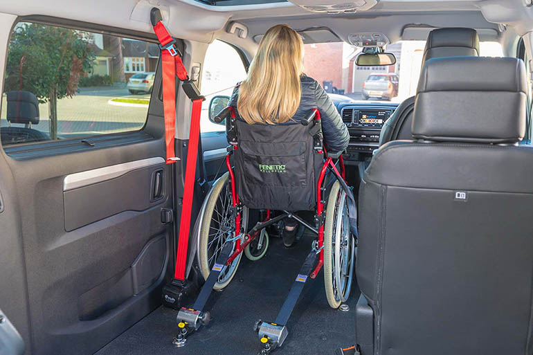 Back view of a person sitting in a wheelchair that is secured with tie-downs. 