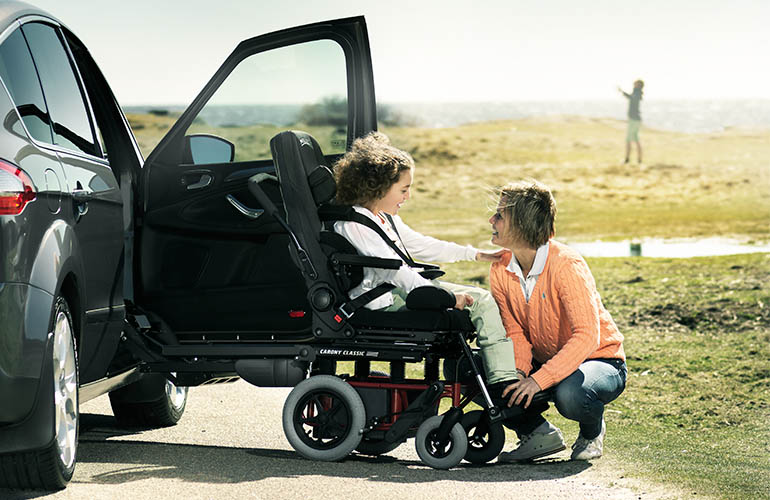 Frau am Strand, die mit einem jungen Mädchen interagiert, das in einem Carony Classic sitzt