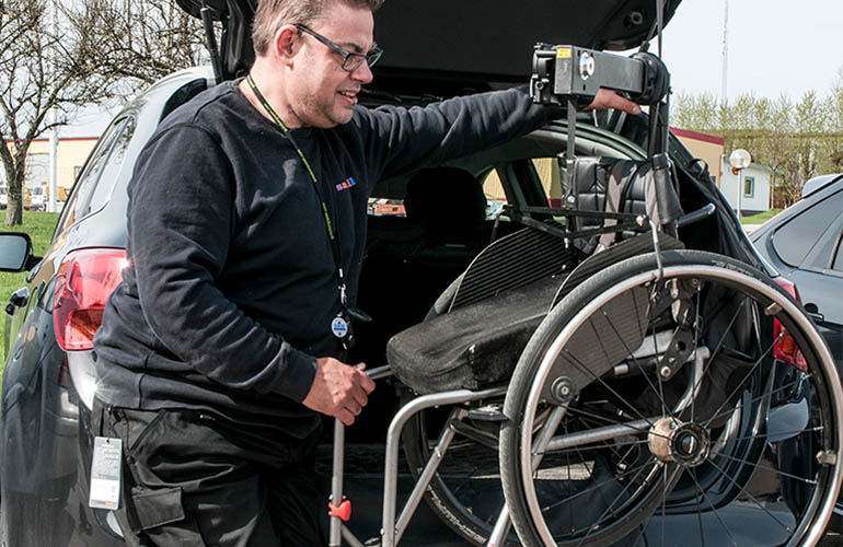 Mann, der einen Rollstuhlaufzug benutzt, um einen Rollstuhl in der Autokabine zu verstauen