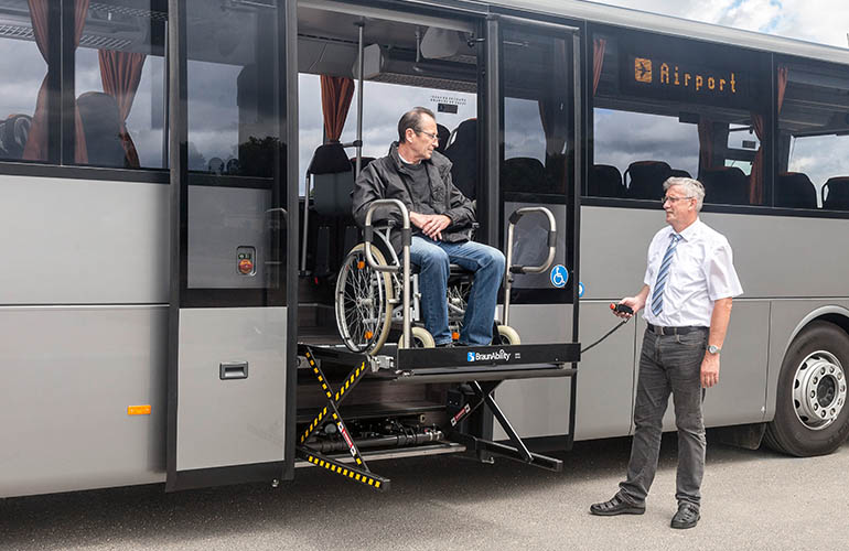 Bus driver assistint a man on a wheelchair into a bus by using a UVL lift