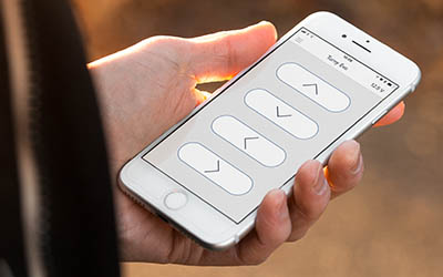 A hand holding a smart phone showing four buttons on the display with arrows in each direction.