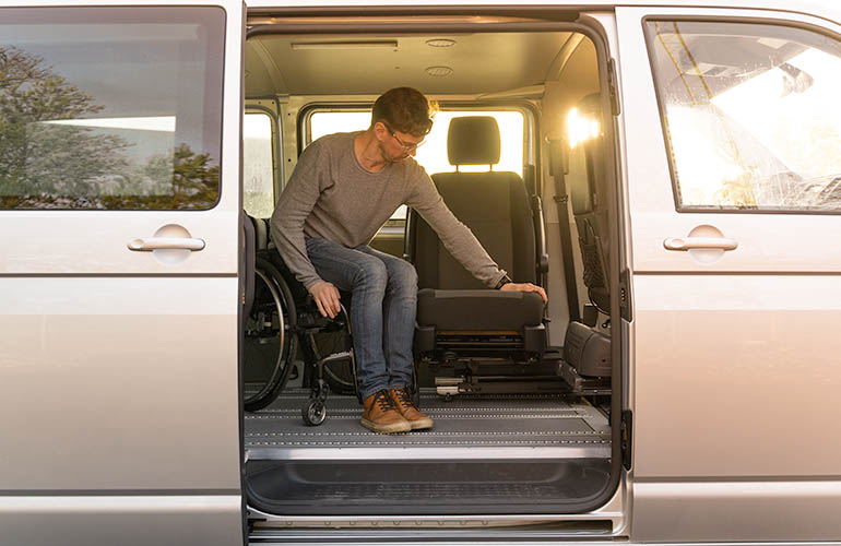 Van with a lateral door open, inside there is a man transfering from the wheelchair to the Turny 6 way