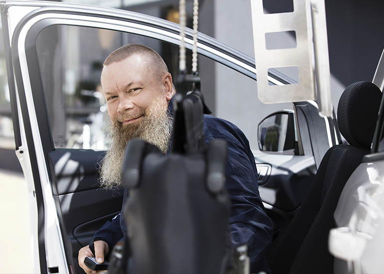 Man smiling behind a wheelchair being retrieved from a chari topper