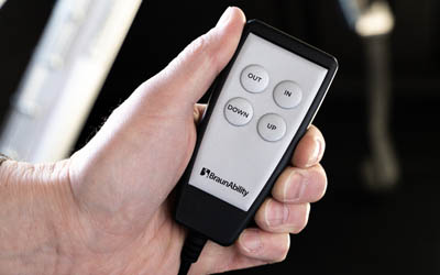 A hand holding a remote control with four buttons titled out, in, down and up.