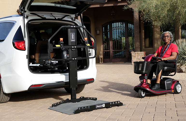 Woman driving her electric wheelchair onto a Joey Lift installed in a car