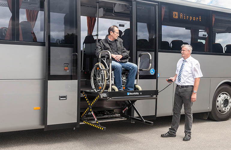 Conducteur aidant une personne en fauteuil roulant à sortir d’un véhicule de transport d’aéroport avec une plateforme élévatrice pour fauteuil roulant