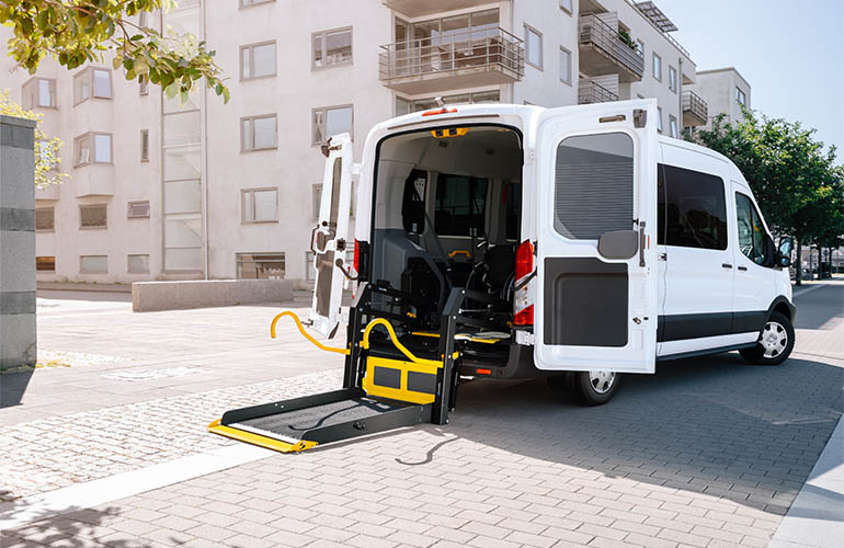 Une camionnette avec des portes arrière ouvertes et un élévateur pour fauteuil roulant déployé.