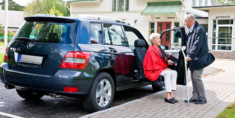 Älterer Mann, der einer älteren Frau hilft, ein Auto mit einem Sitzlift zu verlassen.