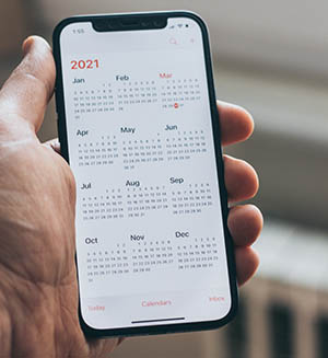 A hand holding a smartphone showing a calendar app.