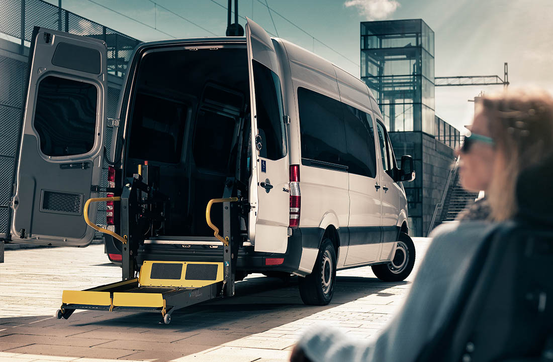 Woman sitting outside a van with a lift lowered from the rear door