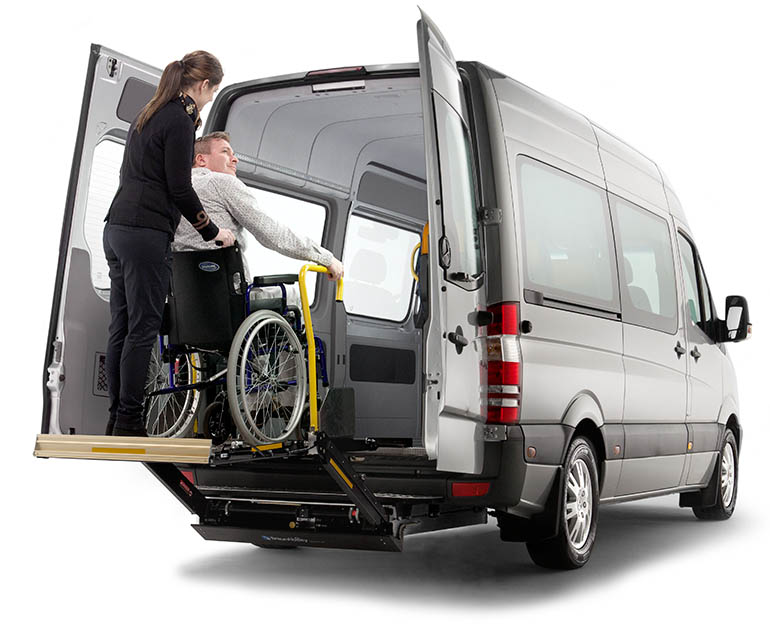 A bus driver assisting a wheelchair user in getting onboard using a wheelchair lift. 