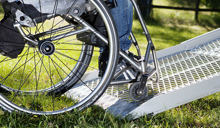 A close-up image of a wheelchair entering a ramp that is folded out in the grass