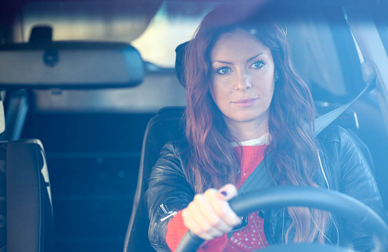 View through a windshield of a woman driving a car. 