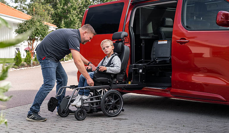Man assisting boy transfer from wheelchair into car