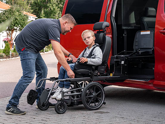 Man assisting boy transfer from wheelchair into car