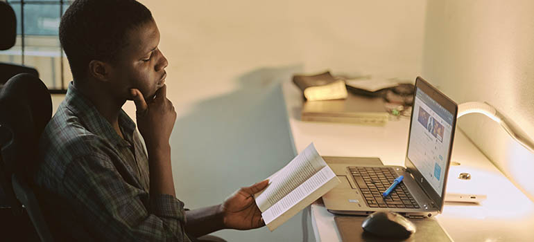 Un homme étudie avec un livre et un ordinateur.