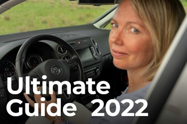 The text "Ultimate Guide 2021" superimposed over a view through a windshield of a woman driving a car. 